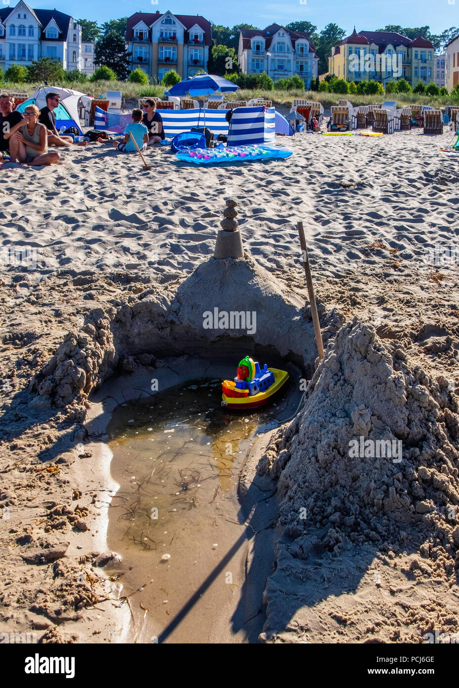 Toy boat & sand castle on crowded Bansin beach as people holiday at the Baltic sea resort on Usedom Island during 2018 Summer heat wave, Heringsdorf,  Stock Photo