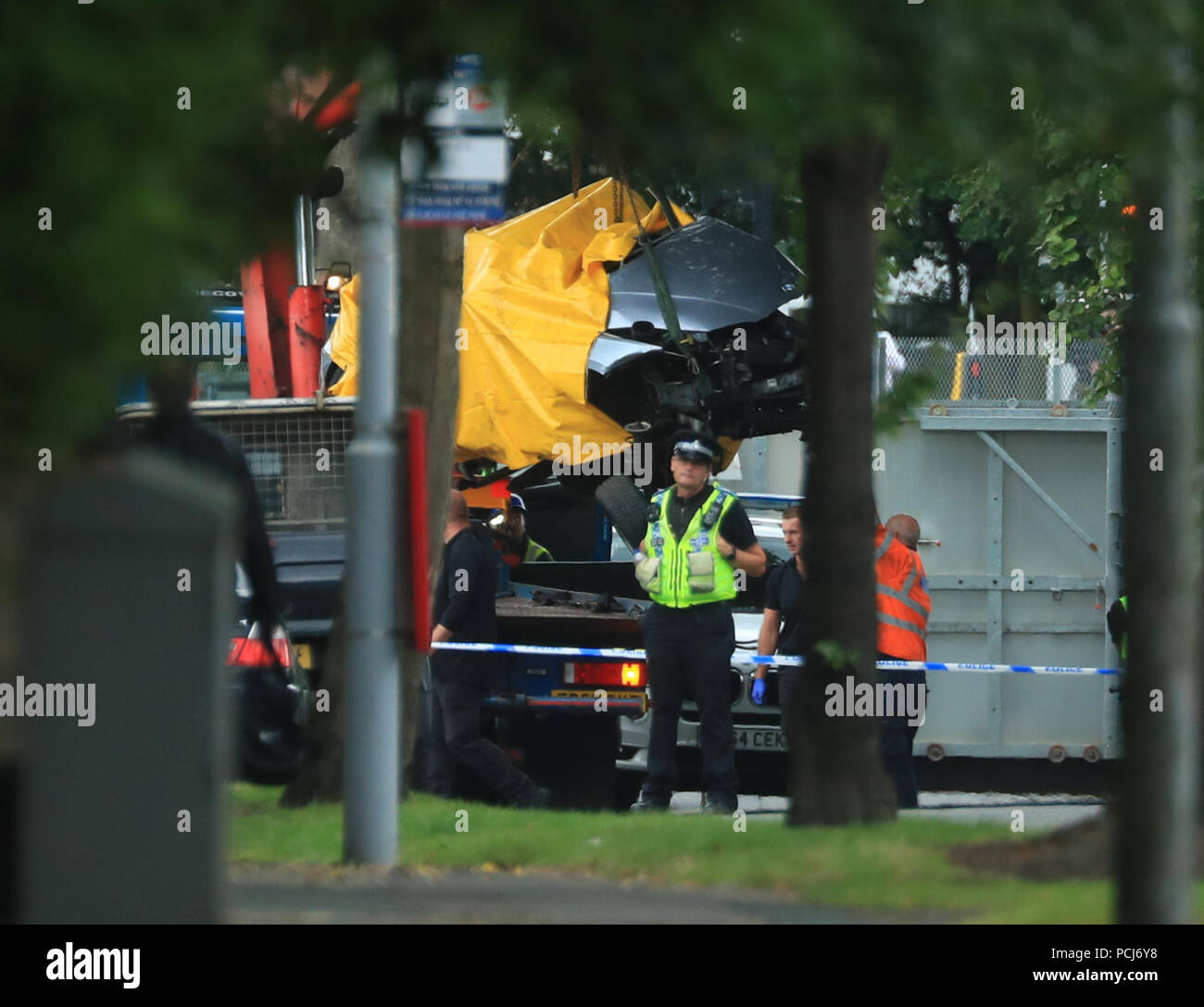 A car covered by a tarpaulin is removed from the scene on Bingley Road at the junction with Toller Lane in Bradford following a road traffic collision where four males died in a car which was being followed by an unmarked police vehicle when it crashed. Stock Photo