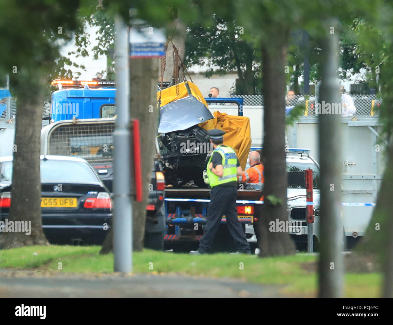 A car covered by a tarpaulin is removed from the scene on Bingley Road at the junction with Toller Lane in Bradford following a road traffic collision where four males died in a car which was being followed by an unmarked police vehicle when it crashed. Stock Photo