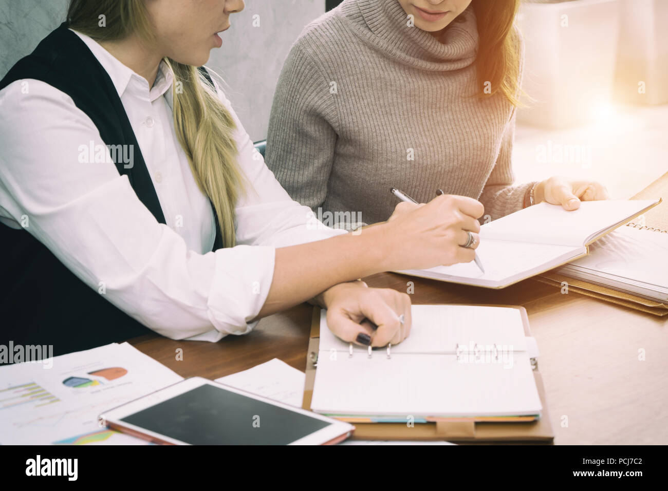 Two hard working young female entrepreneurs working together on office desk reading report with serious engrossed expressions. Stock Photo