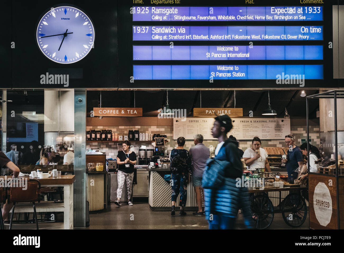 People sitting at a cafe, waiting for their trains under the departure board inside St. Pancras station, London, UK. Stock Photo