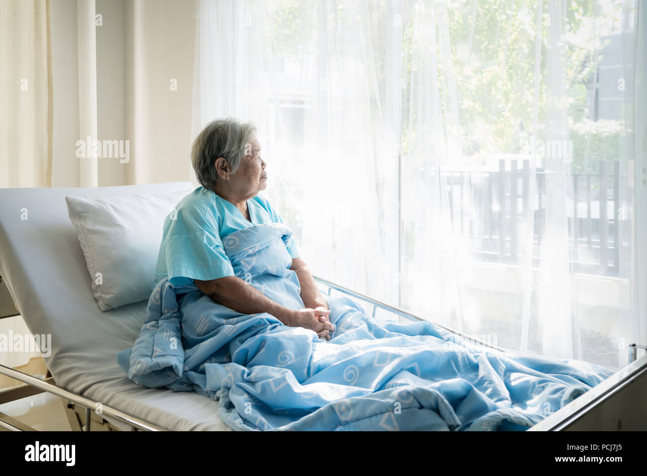 Asian depressed elderly woman patients lying on bed looking out the window in hospital. Elderly woman patients is glad recovered from the illness. Stock Photo