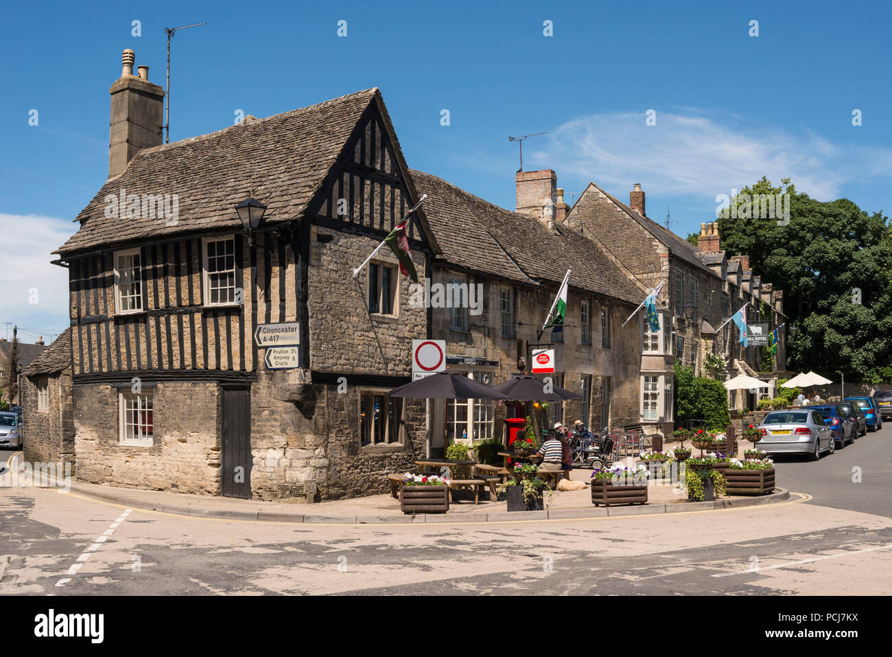 People sitting outside of Old Cotswold stone buildings in Market Place, Fairford, Gloucestershire, UK Stock Photo