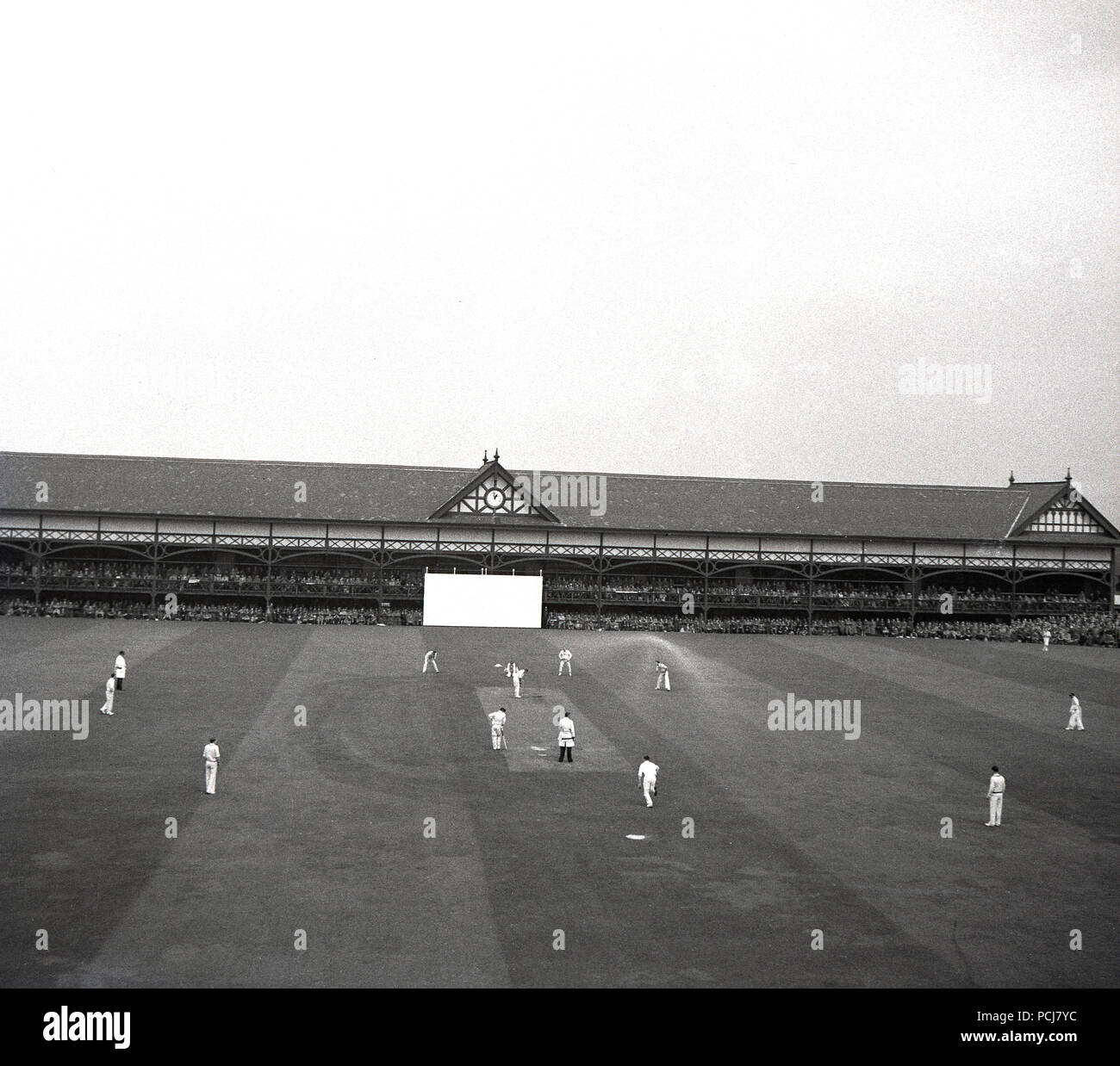 1958, phistorical, county cricket match, England, showing the players out in the field, and on the far side of the ground, the long two-storey traditional wooden-built pavilion for the viewing spectators. Stock Photo