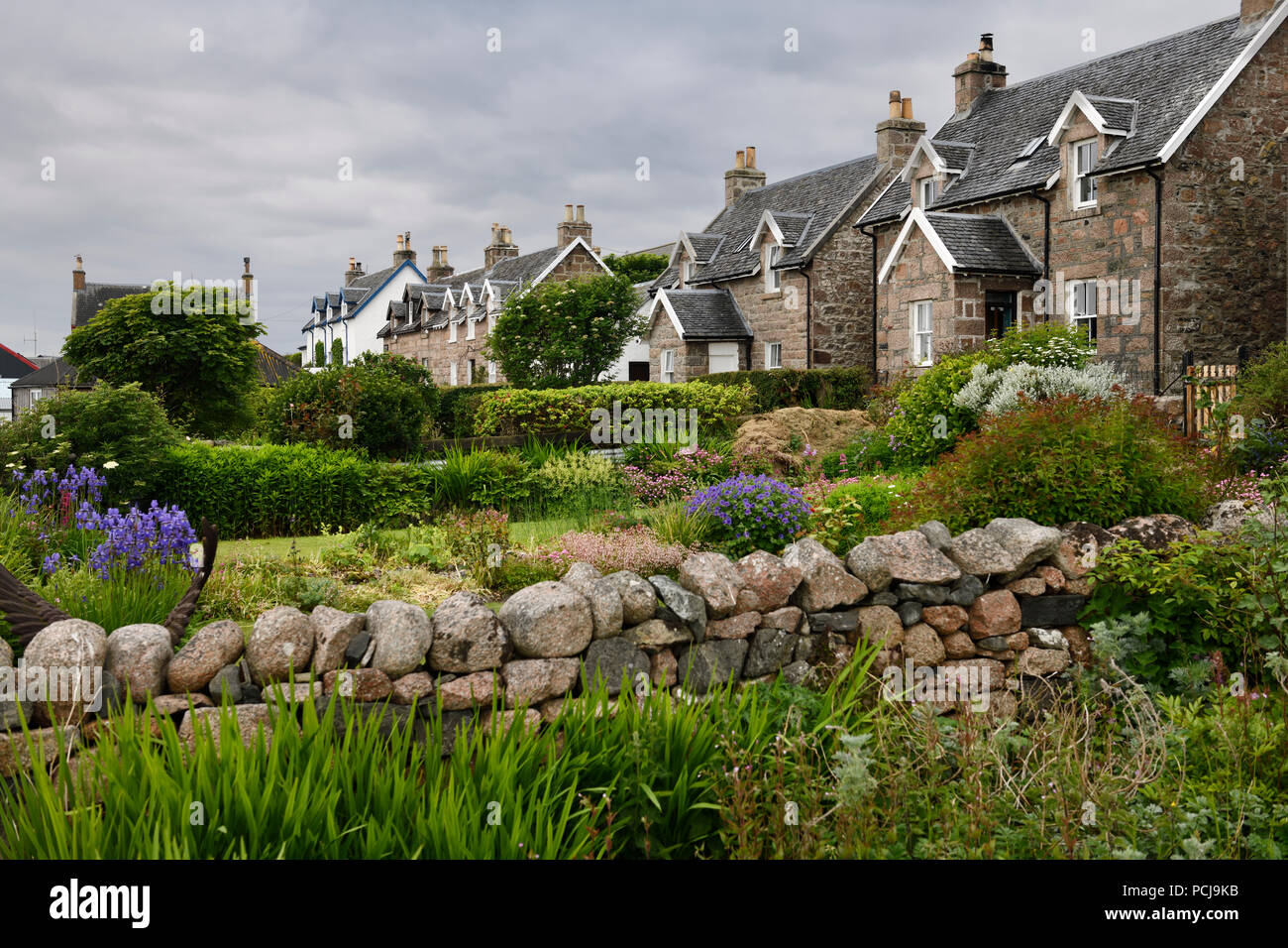 Flower gardens under cloudy sky with stone houses of Baile Mor village on Isle of Iona Scotland UK Stock Photo