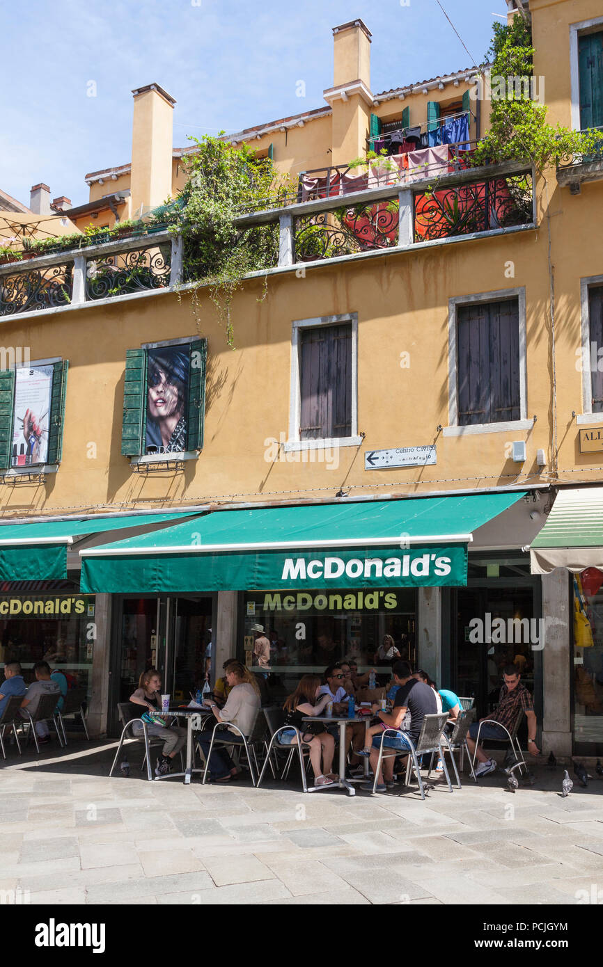 People eating at tables outside McDonald's restaurant, Cannaregio, Strada Nuova, Venice, Veneto, Italy in summer Stock Photo