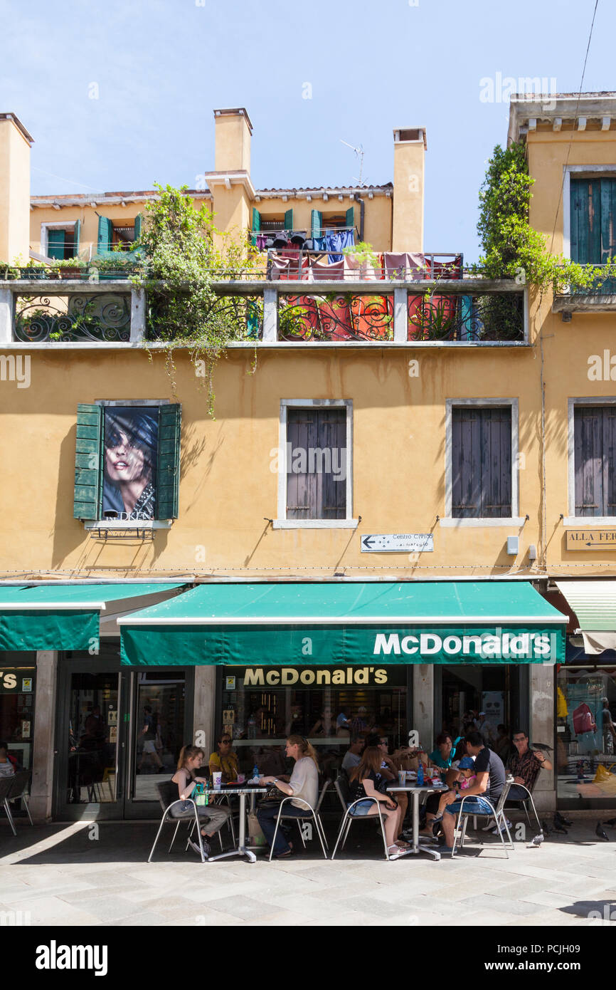 People eating at tables outside McDonald's restaurant, Cannaregio, Strada Nuova, Venice, Veneto, Italy in summer Stock Photo