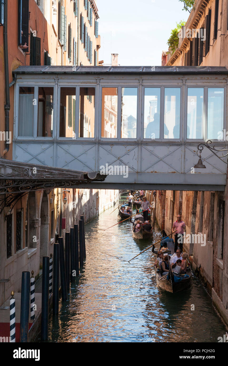 Gondolas with tourists in a narrow canal Castello, Venice, Veneto, Italy passing under a covered skywalk between the Danieli Hotel palazzos Stock Photo