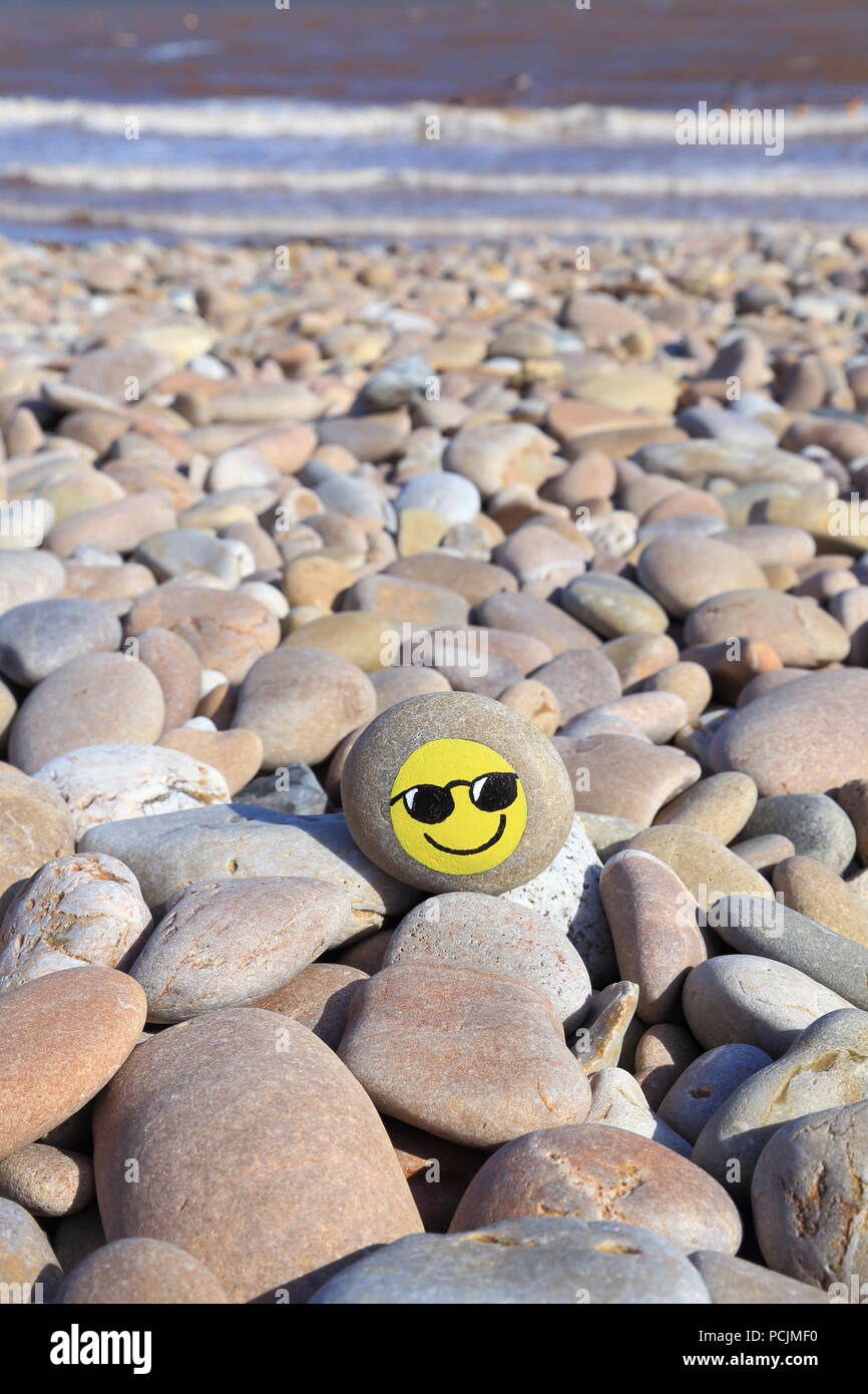 Stone with painted smiley face on the pebble beach of the Jurassic Coast in Devon Stock Photo