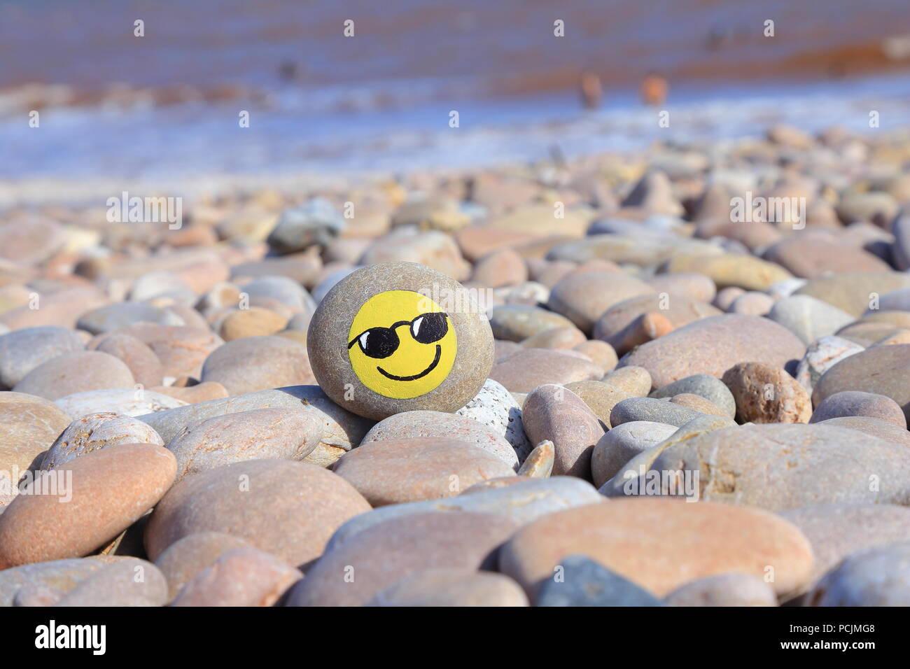 Stone with painted smiley face on the pebble beach of the Jurassic Coast in Devon Stock Photo