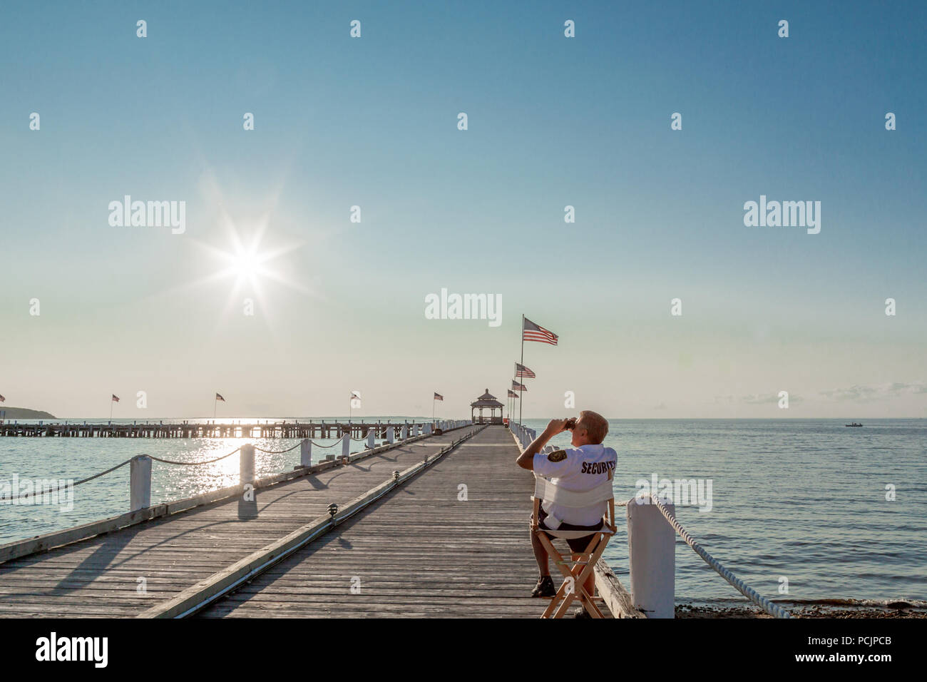 security guard sitting in a chair looking through binoculars on a pier in Montauk, NY Stock Photo