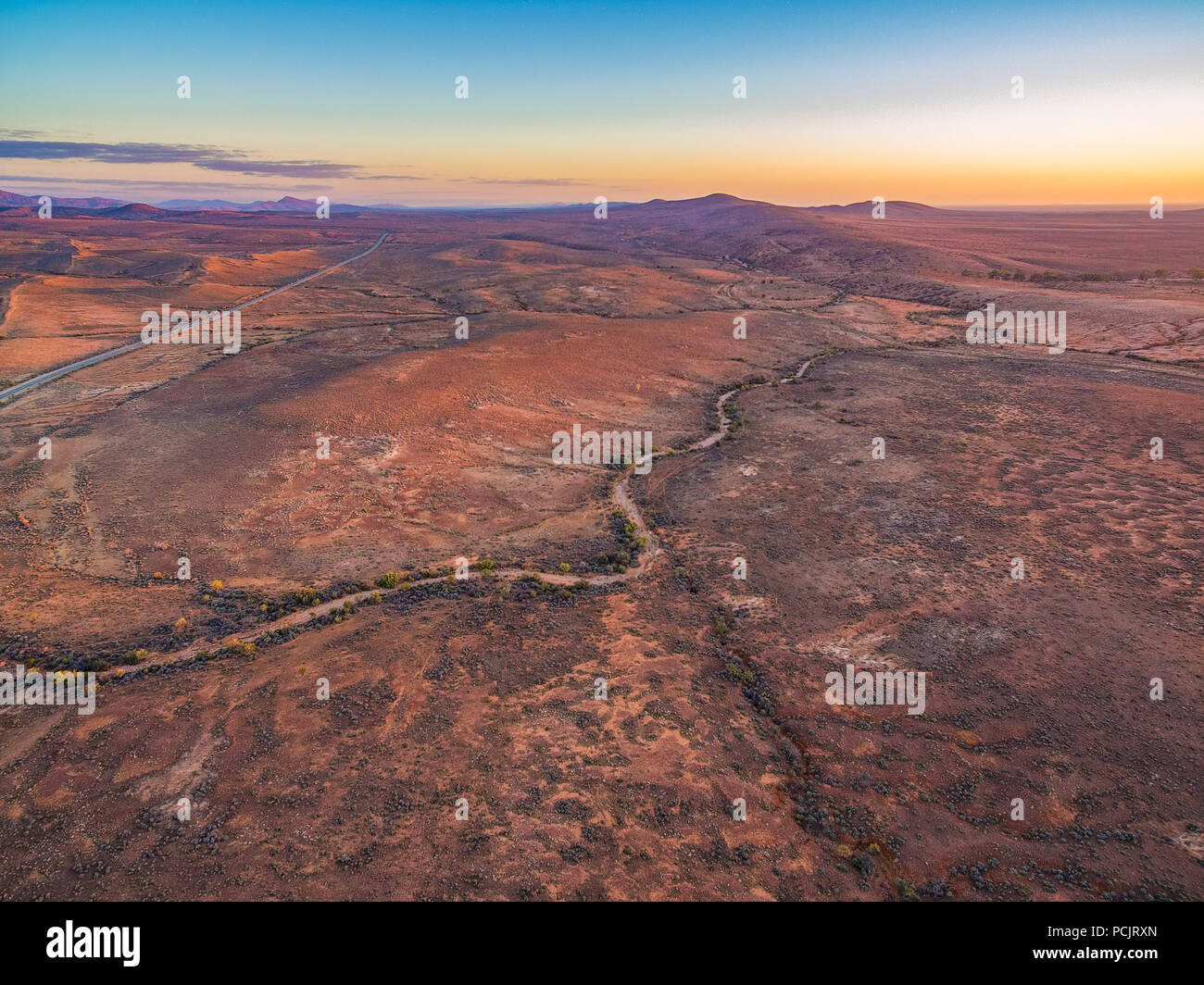 Aerial view of sunset over alien martian-like red landscape with winding gravel road Stock Photo