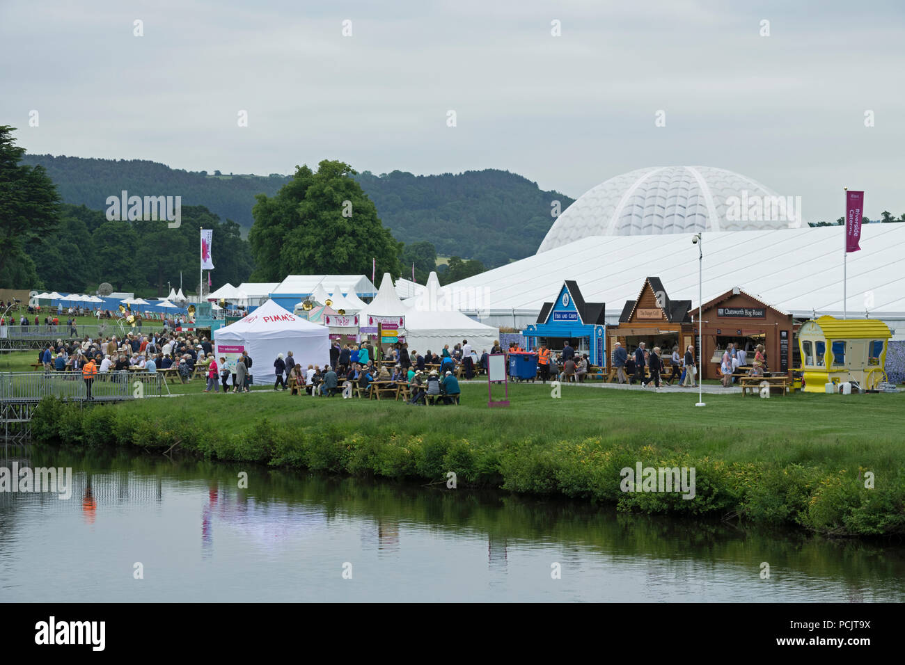 Large crowd of people at showground, many sitting by refreshment trade stands & marquee at busy RHS Chatsworth Flower Show, Derbyshire, England, UK. Stock Photo