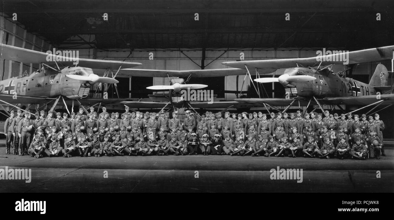 Image from the photo album of Oberleutnant Wilhelm Gaul: Kriegsmarine and Luftwaffe personnel of 1. Staffel, Küstenfliegergruppe 106 pose in front of two of the unit's Heinkel He 60 floatplanes in 1939. The aircraft now bear wartime codes and the distinctive Staffel Badge of three dice and a shaker on a black shield. The unit went to war in these aircraft before rapidly converting to the more capable Heinkel He 115. Stock Photo