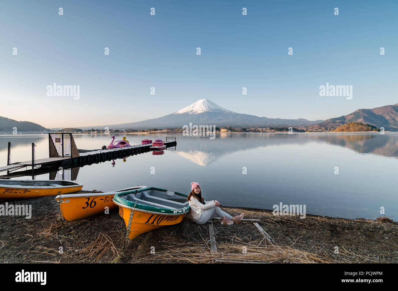 Portrait of beautiful Asian girl post at the Nothern Shore of Lake Kawaguchiko. Mountain Fuji with clear reflection can be see at the background. Stock Photo
