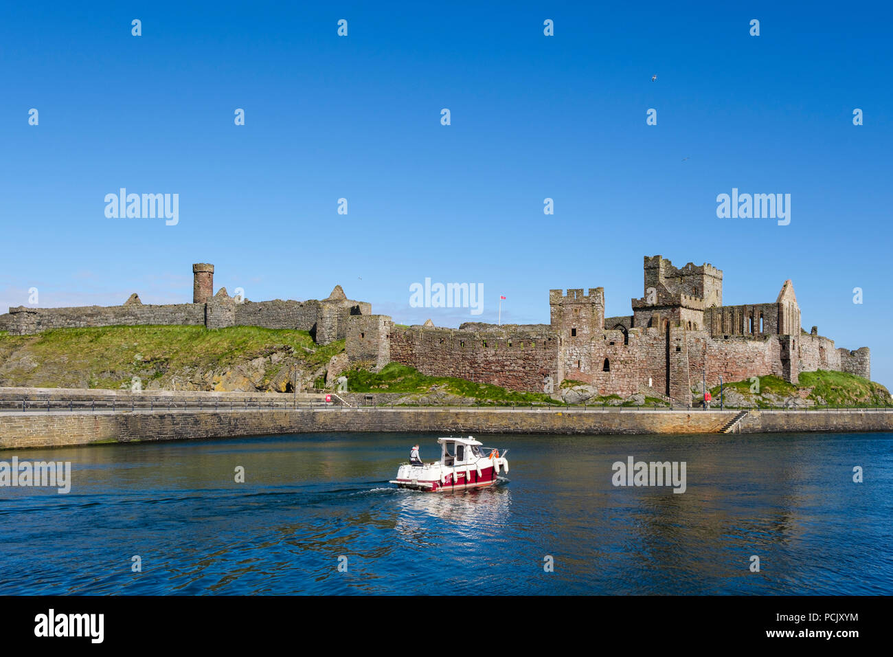 Peel castle ruins with boat heading out to sea from harbour. Peel, Isle of Man, British Isles Stock Photo