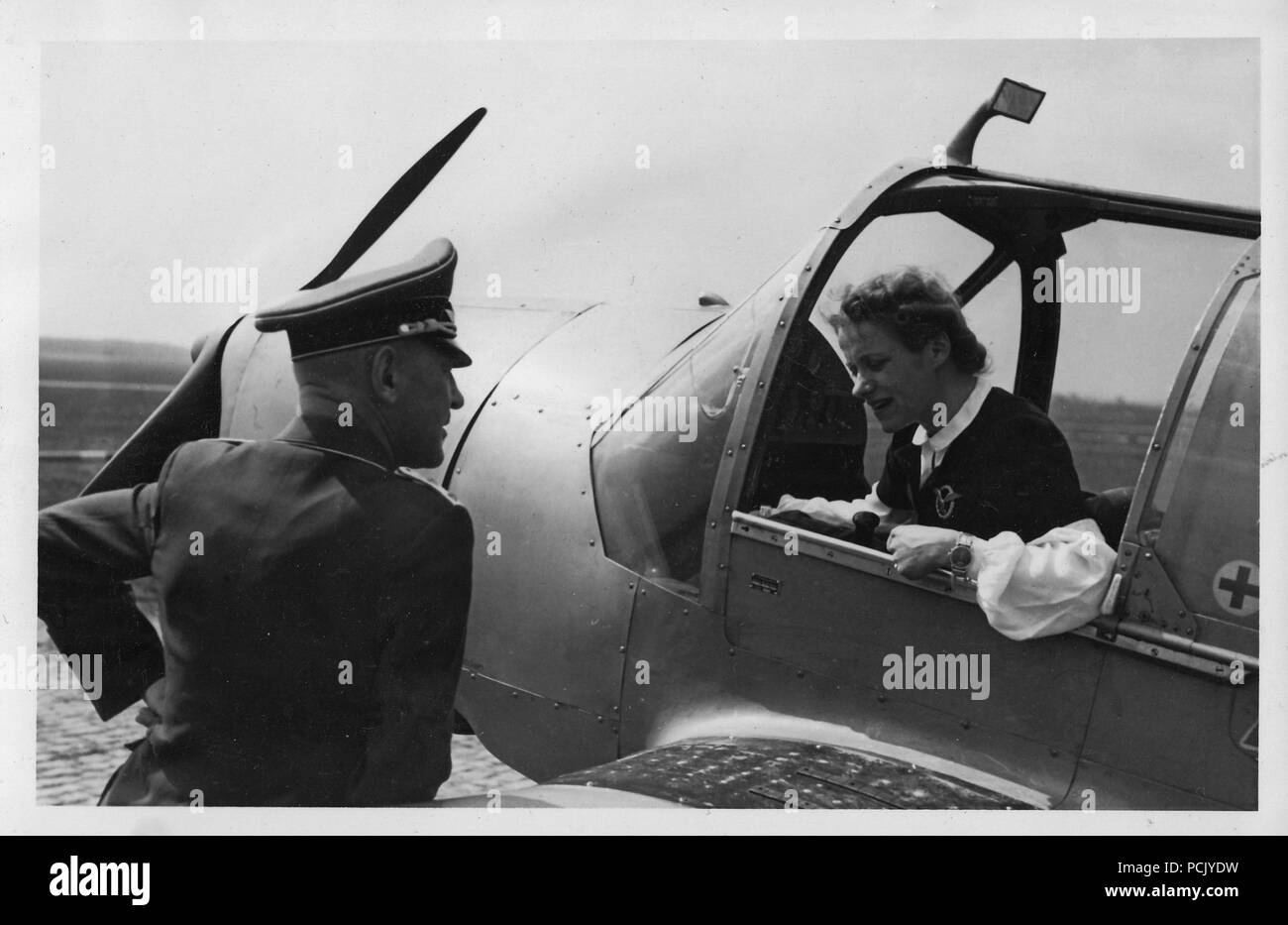 Image from a photo album relating to II. Gruppe, Jagdgeschwader 3: Flugkapitän Hanna Reitsch in the pilot seat of a Messerschmitt Bf108 'Taifun' engages in conversation with a Luftwaffe Hauptmann of JG3. In this image Hanna Reitsch wears an example of the standard Luftwaffe Pilots' Award Badge. She would later be one of only two recipients of the Combined Pilot & Observer Badge with Diamonds for Women. Stock Photo