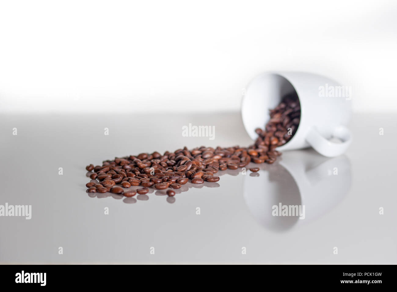 Many coffee coffee beans spilling out of a cup on a white counterspace with textspace Stock Photo