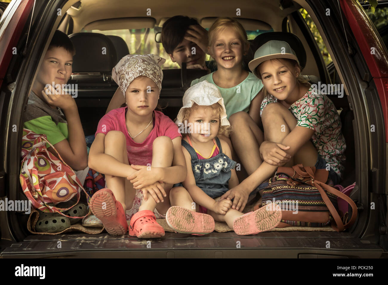 Group of smiling children big family in car trunk luggage going to road
