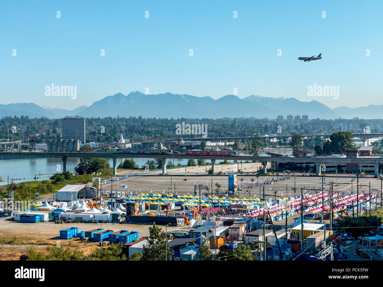 Richmond Night Market by day. Fraser River is on left. Richmond, BC, Canada. Canada Line Skytrain can be seen on its route between downtown Vancouver and Vancouver International Airport. And a jet can be seen on its landing approach to the airport.The market is open weekends and holiday Mondays during summer. Stock Photo