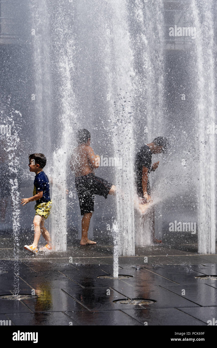 Children cooling off playing in water fountains in on Rue Jeanne Mance in Montreals Entertainment District. Taken during the 2108 heatwave. Stock Photo