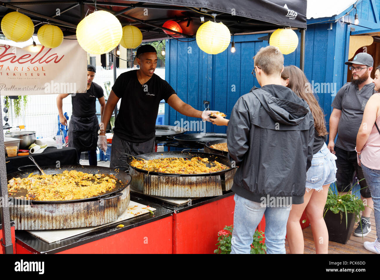 A young man serving paella to a lady customer at an outdoor street food kiosk at Bouffons Montreal Stock Photo