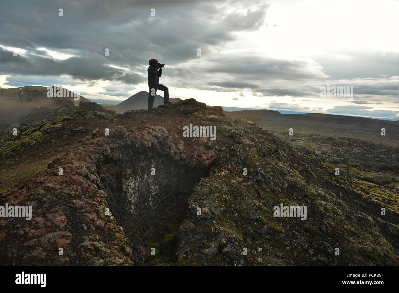 An adventurous photographer climbs up Krafla Volcano and taking photos of lava ruins in the sunset Stock Photo