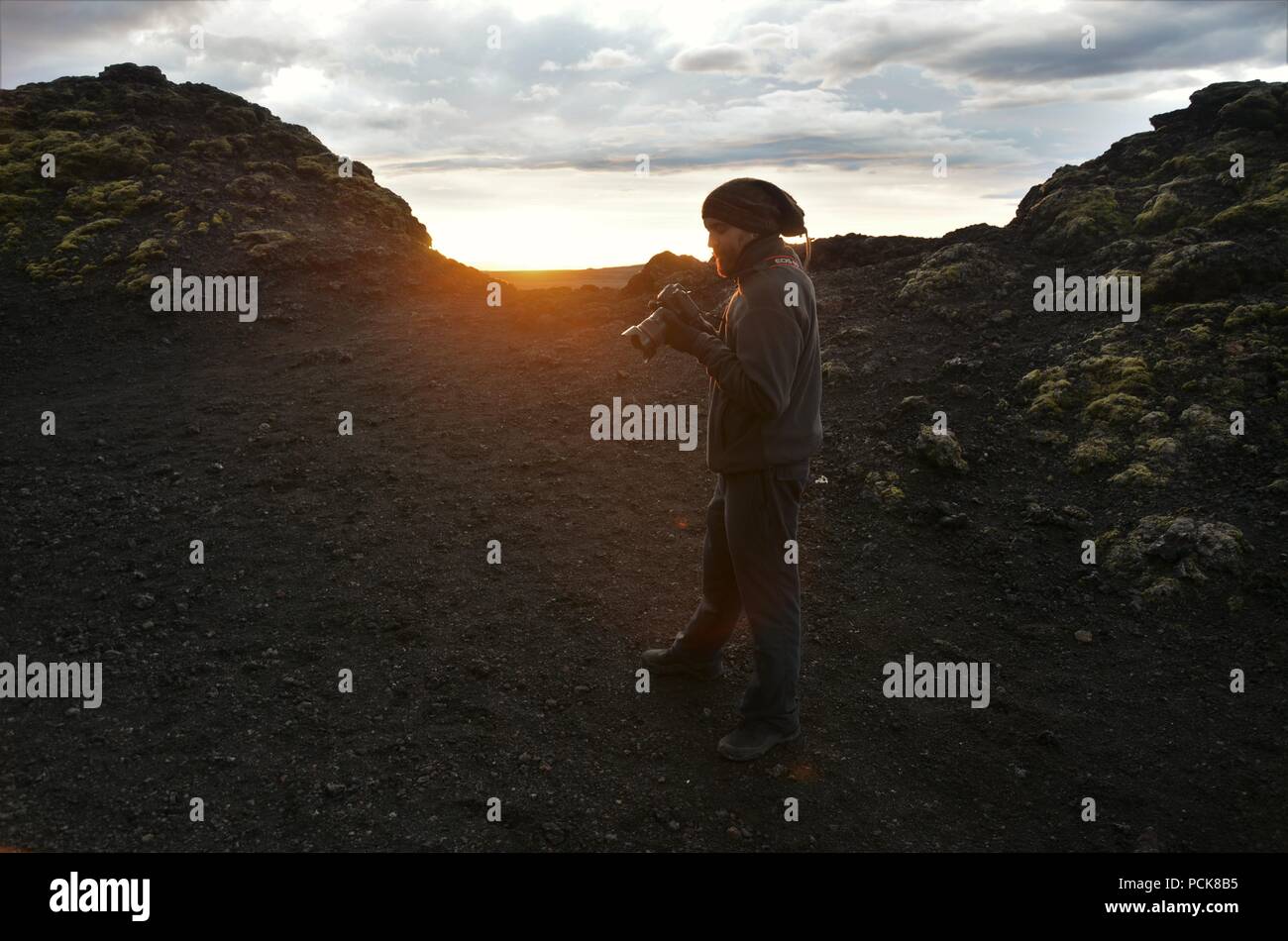 An adventurous photographer climbs up Krafla Volcano and taking photos of lava ruins in the sunset Stock Photo