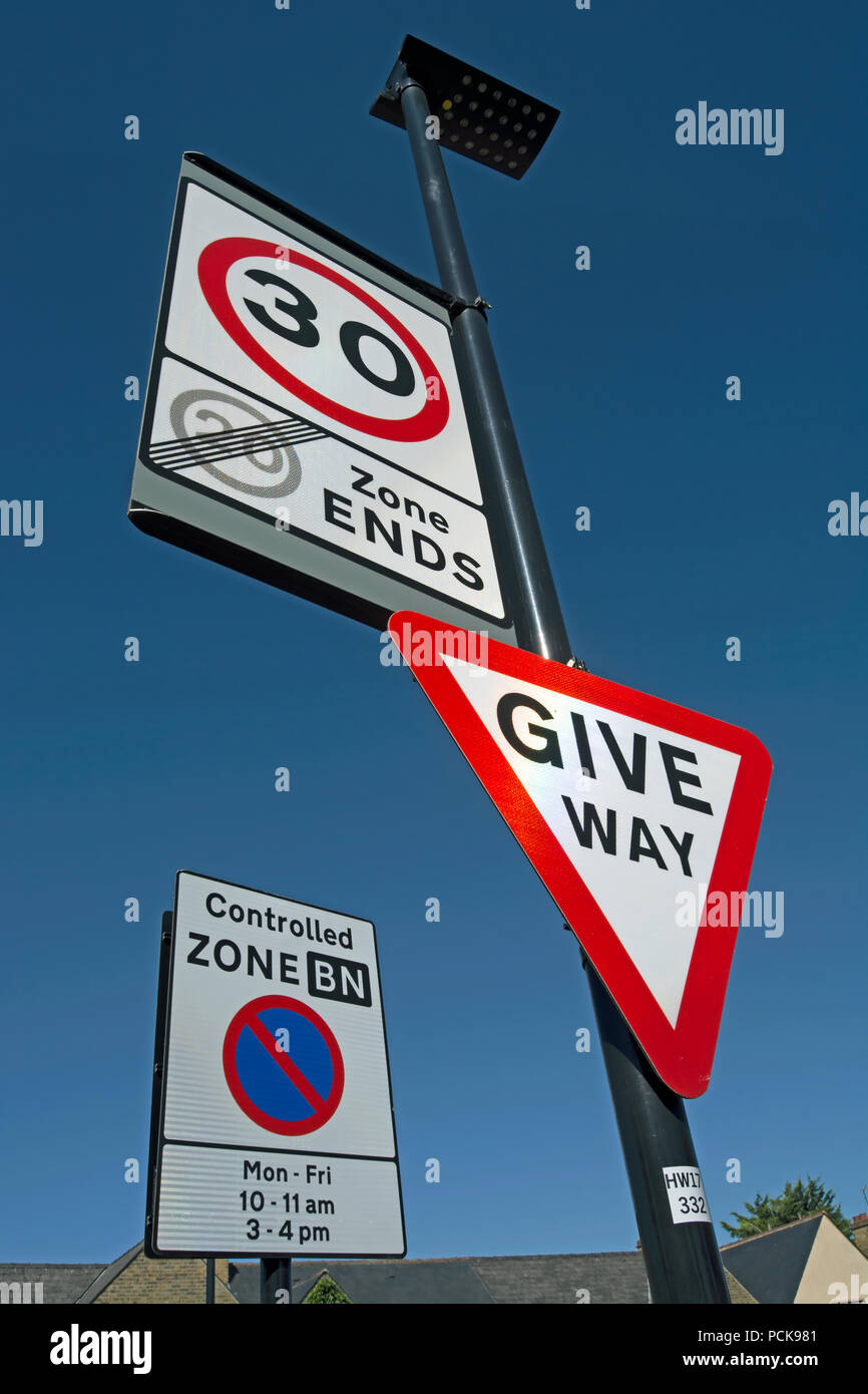 british road signs indicating give way, the start of a 30mph speed limit and the end of a 20mph speed limit zone, with controlled parking sign to rear Stock Photo