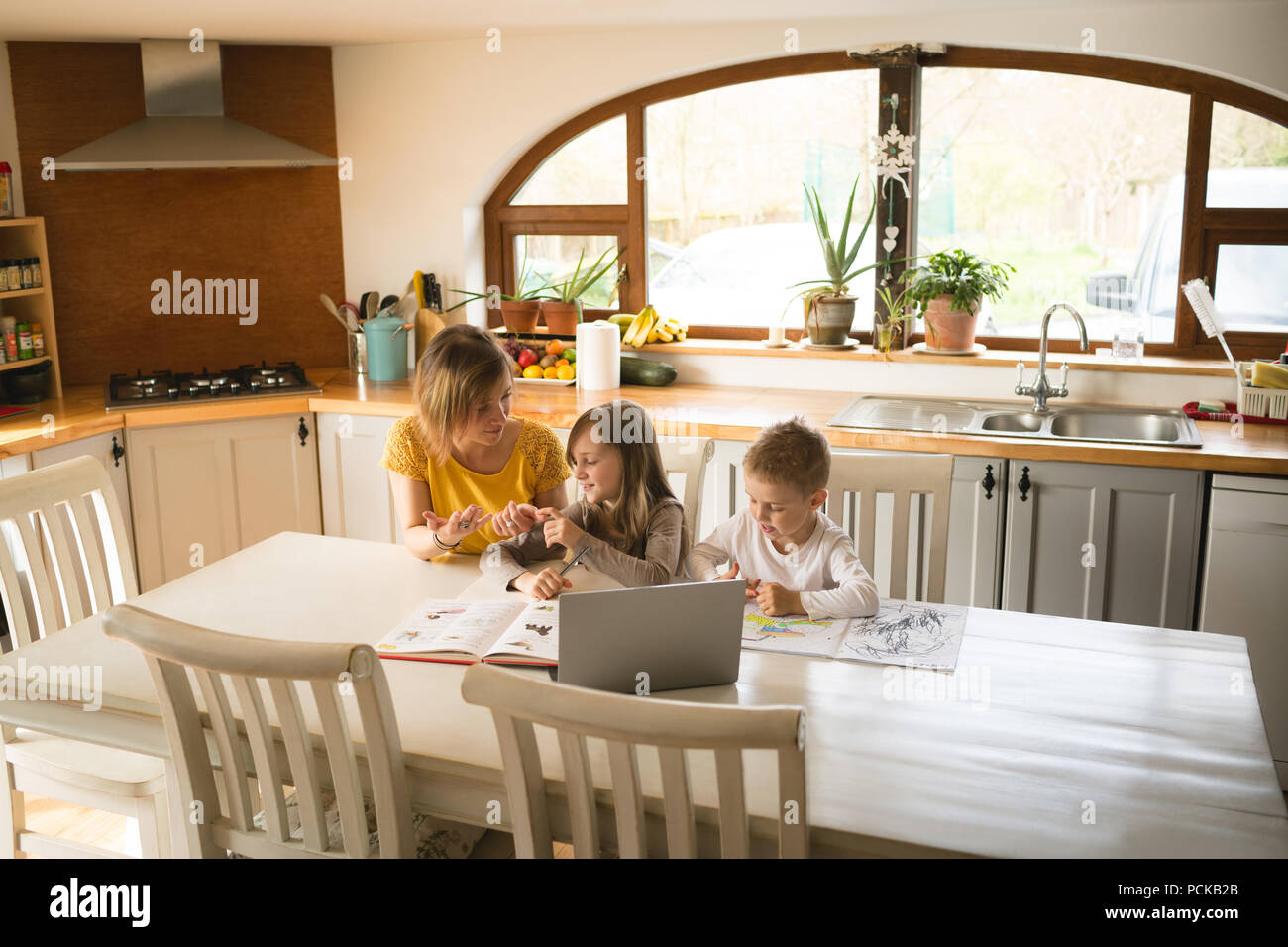 Mother helping children with homework in kitchen Stock Photo