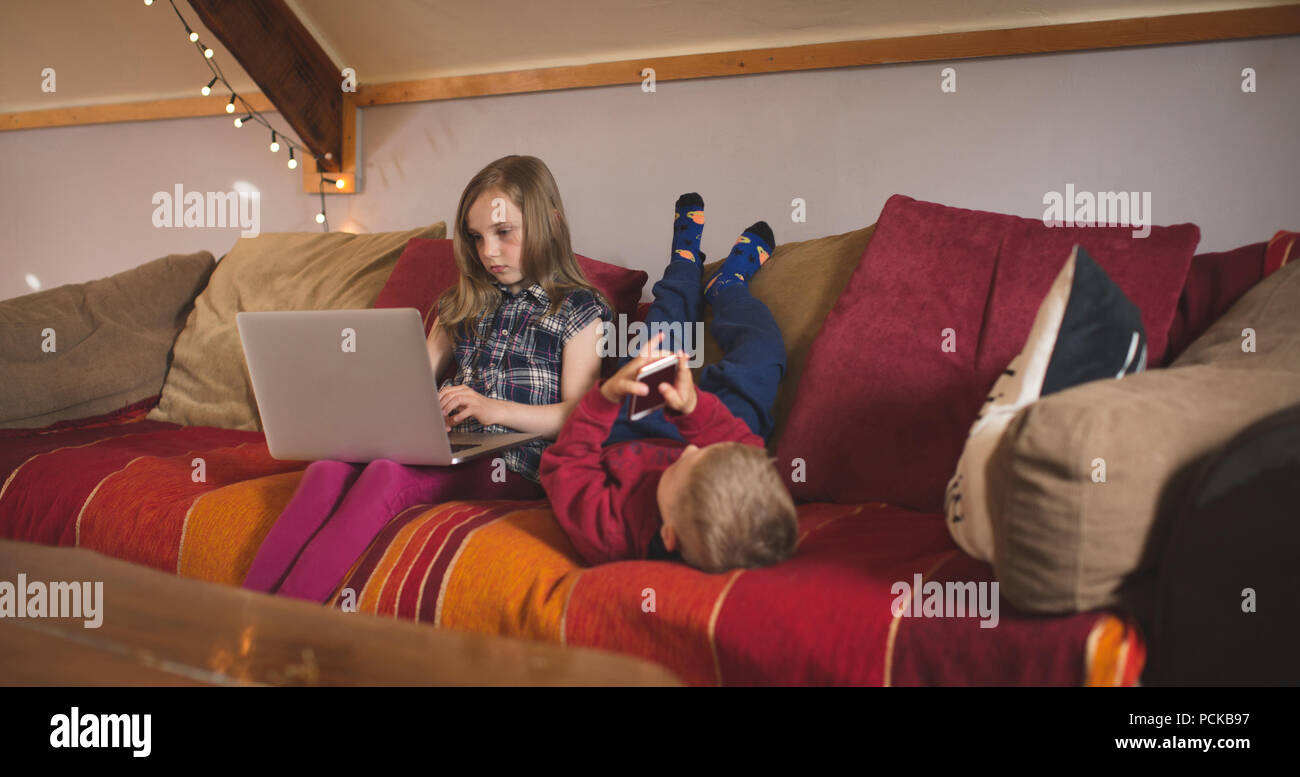 Sibling using multimedia devices on sofa Stock Photo