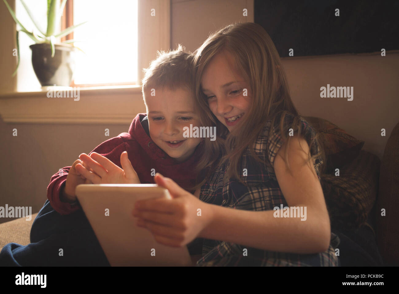 Sibling using tablet on sofa at home Stock Photo