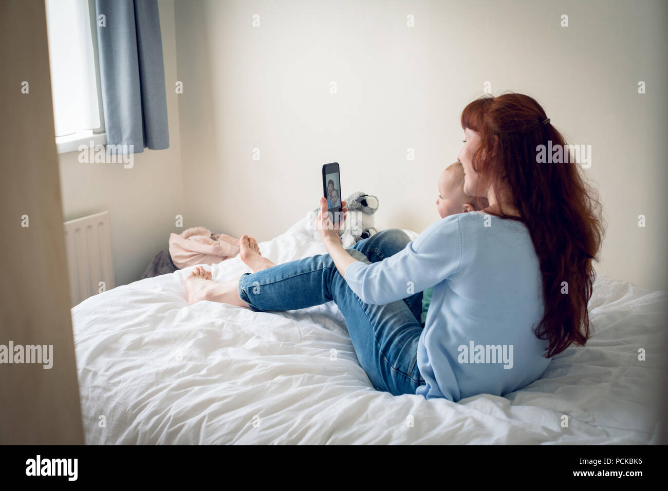 Mother and baby girl taking selfie with mobile phone in bedroom Stock Photo