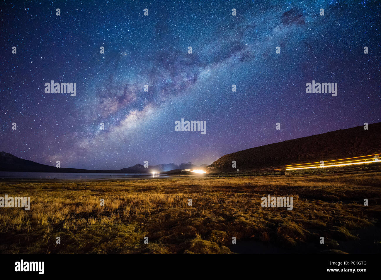 Starry sky with Milky Way on Lake Chungará, light trails of trucks from Bolivia, Nevados de Quimsachata, Lauca National Park Stock Photo