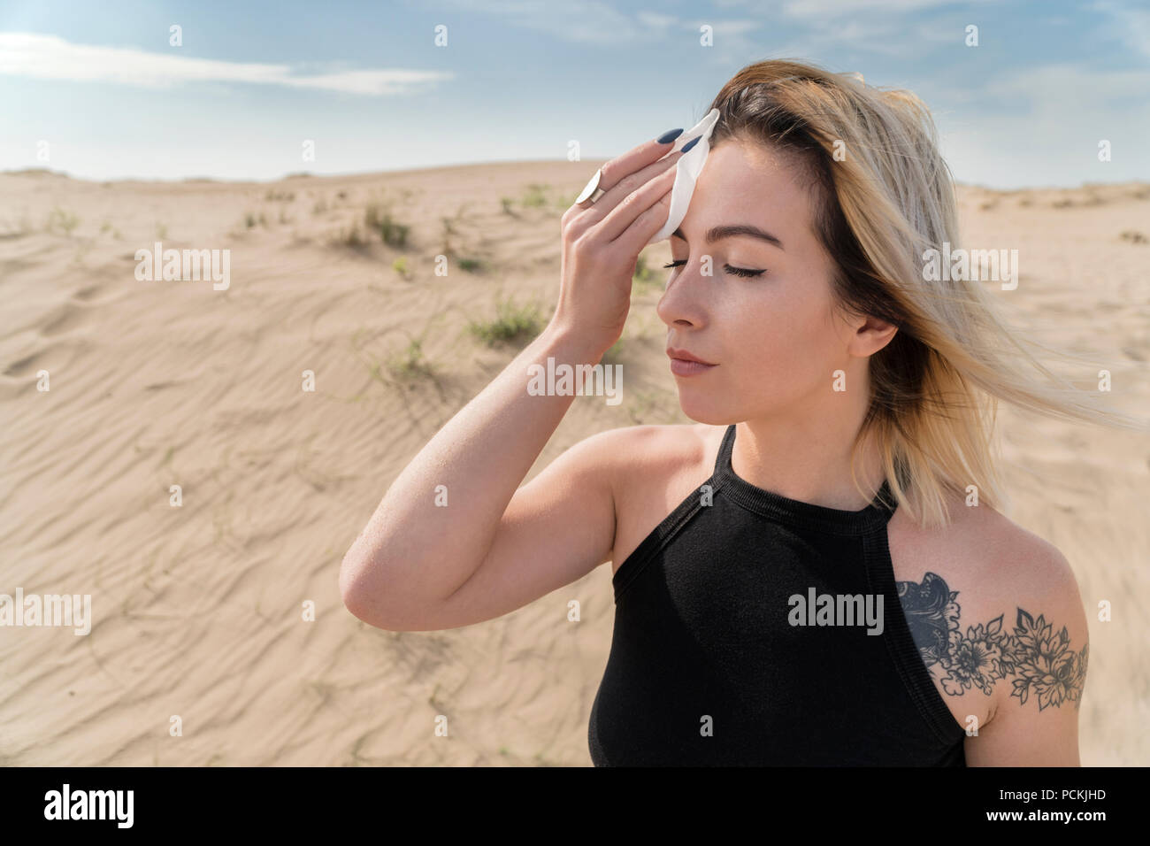 Portrait of a woman on a sunny day in the desert, wiping the sweat from her forehead with a handkerchief Stock Photo