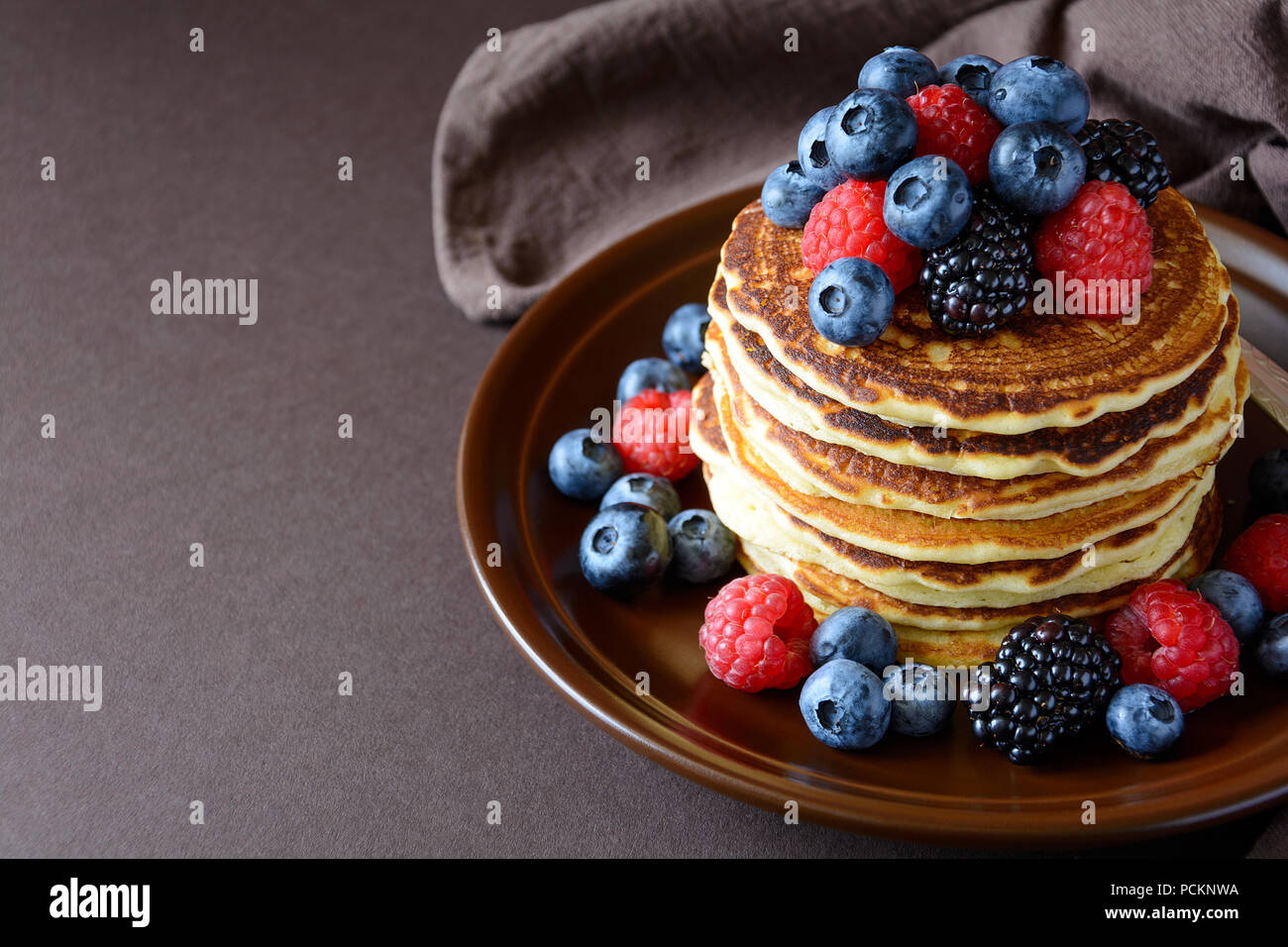 Stack of pancakes with fresh blueberry, raspberry and blackberry on brown plate Stock Photo