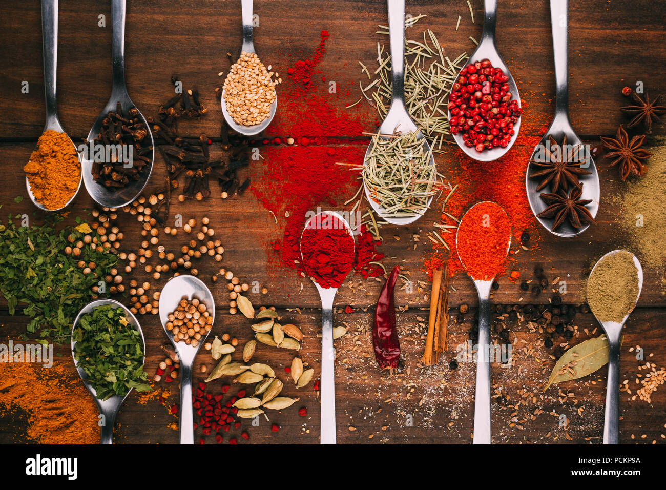 Top view of wooden table full of spices in spoons, you can see the most popular condiments and seasoners Stock Photo
