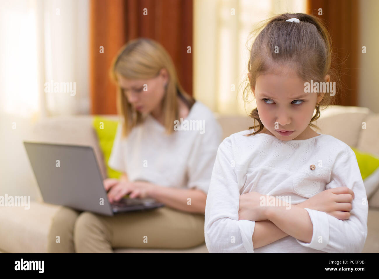 Sadness young girl. Portrait of bored daughter with mother using cellphone on sofa. Stock Photo