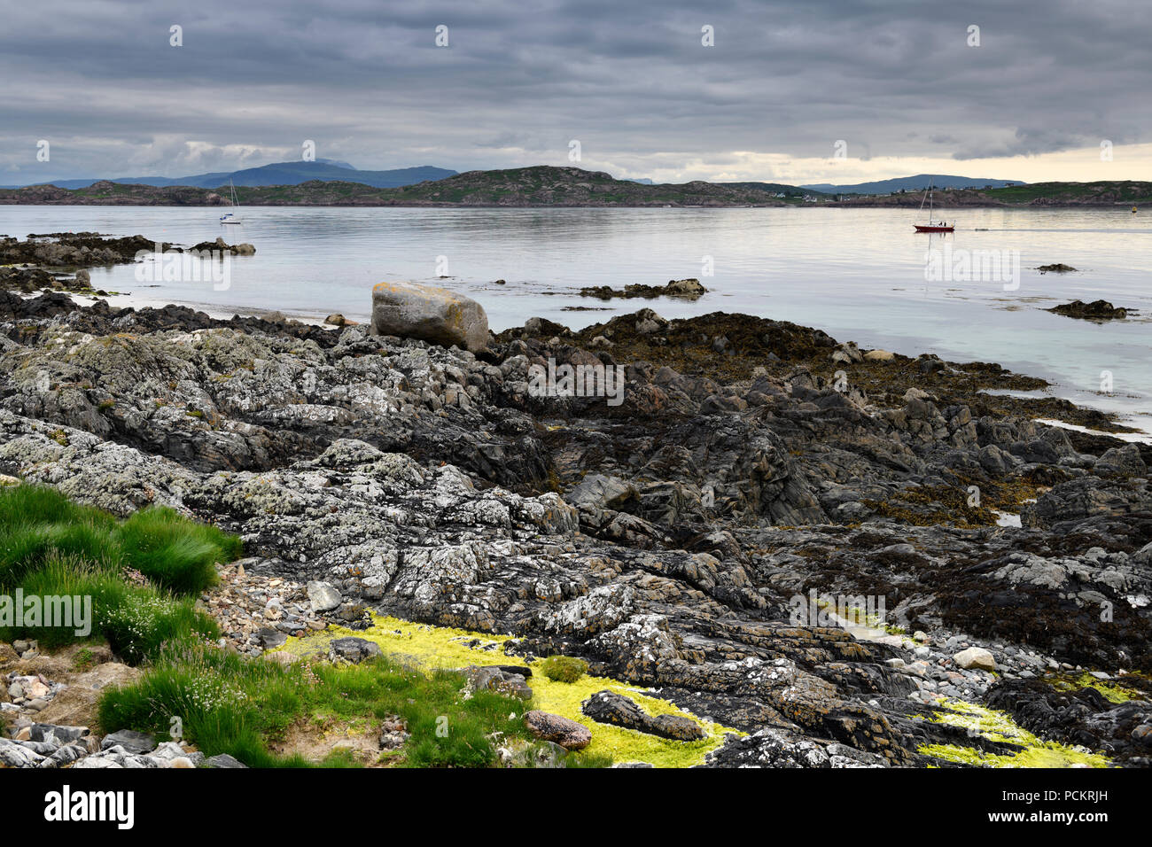 Rocky shore of Isle of Iona with sailboats on Sound of Iona and view of