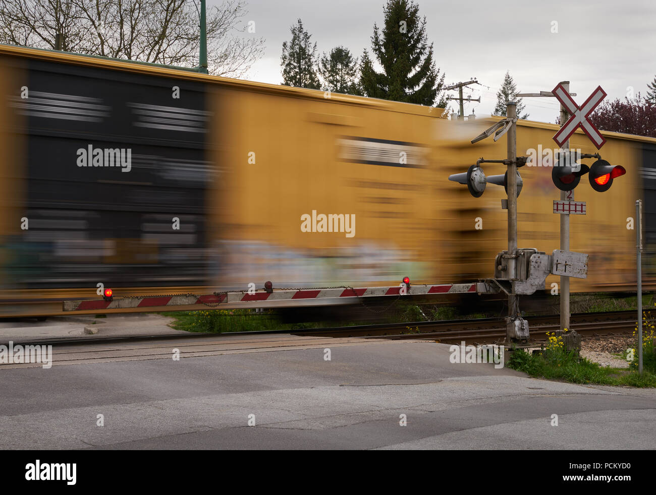 Street Level Railway Crossing .  A train passes a level train crossing with the crossing arms down and lights flashing. Stock Photo