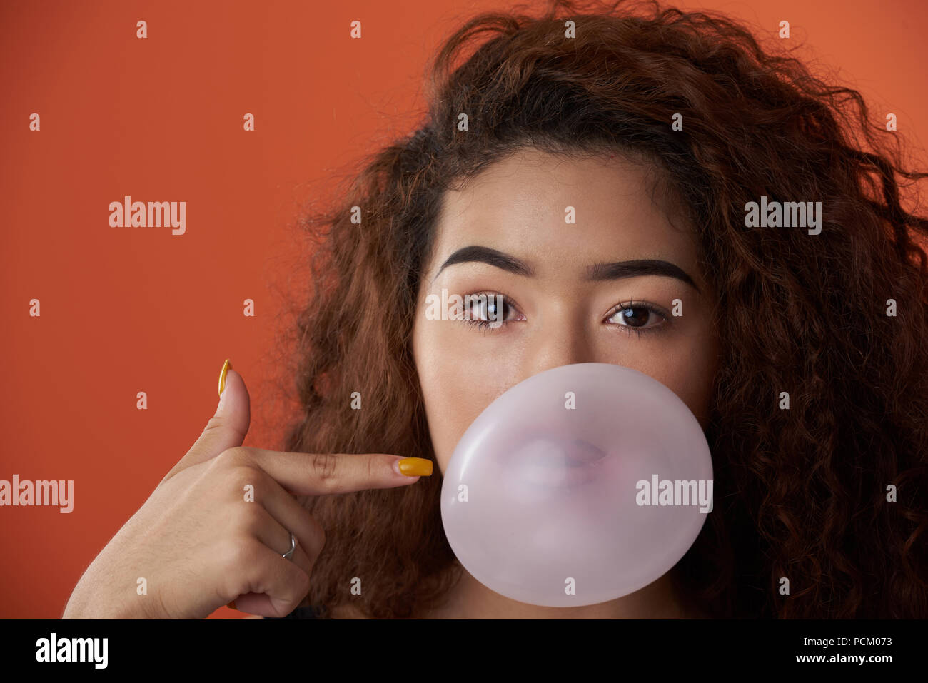 Headshot of woman with bubble gum ball in studio orange color background Stock Photo