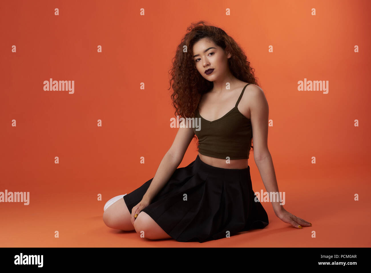 Young latina woman in casual outfit sitting on orange color Stock Photo -  Alamy