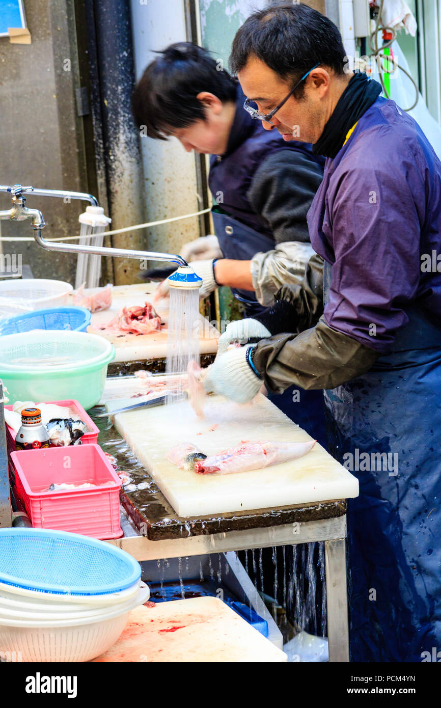 Kuromon Ichiba, Osaka's kitchen food market. Two men, standing while slicing fish up, working on table with running water flowing off the end. Stock Photo