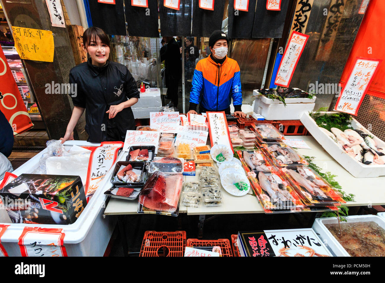 Kuromon Ichiba, food market in Osaka. Fish monger stall with fish and seafoods prepacked in plastic containers, two shop workers standing facing. Stock Photo