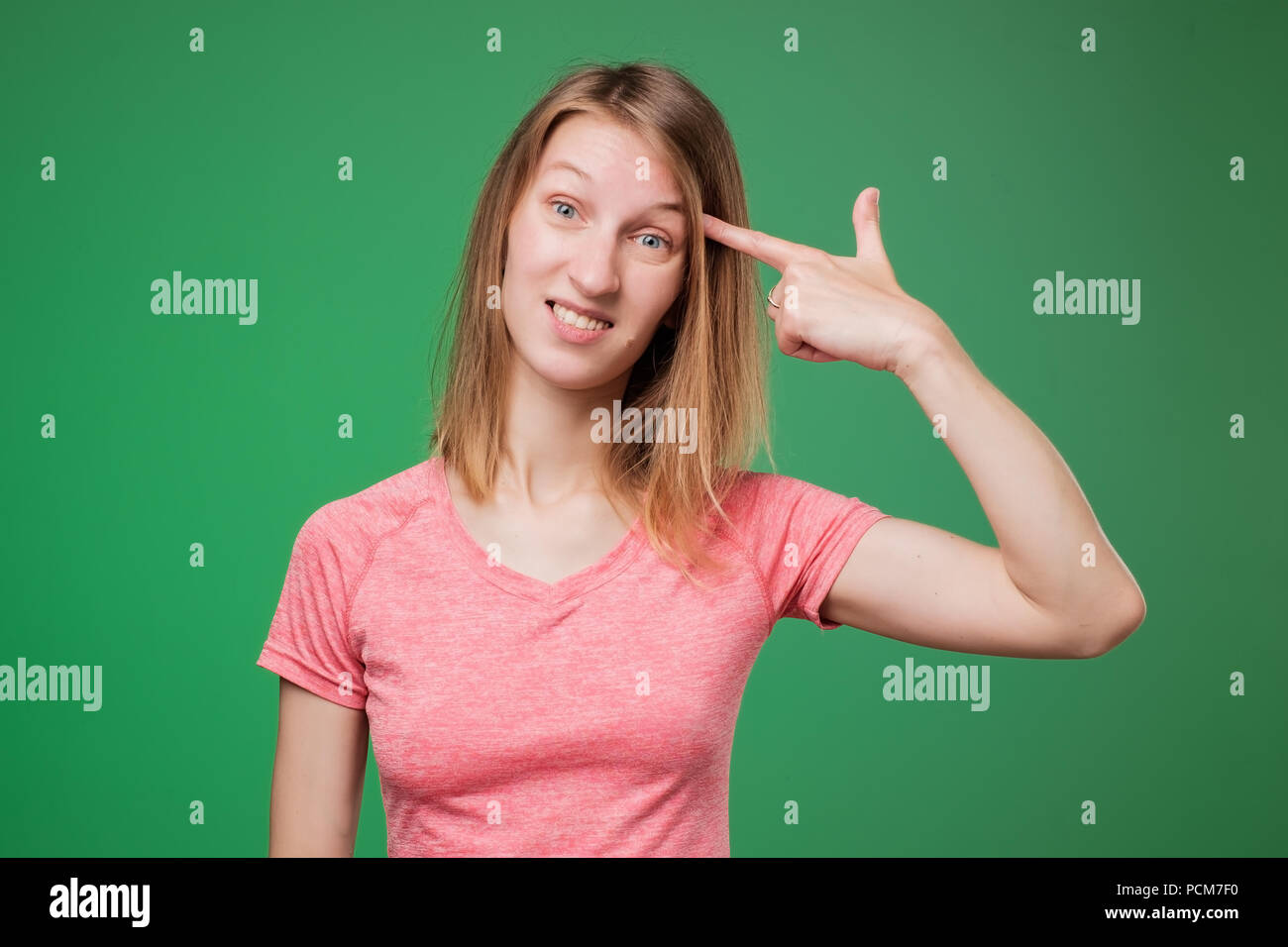 Image of european woman emotionally putting fingers to her temple like gun, being puzzled over green wall. Stock Photo