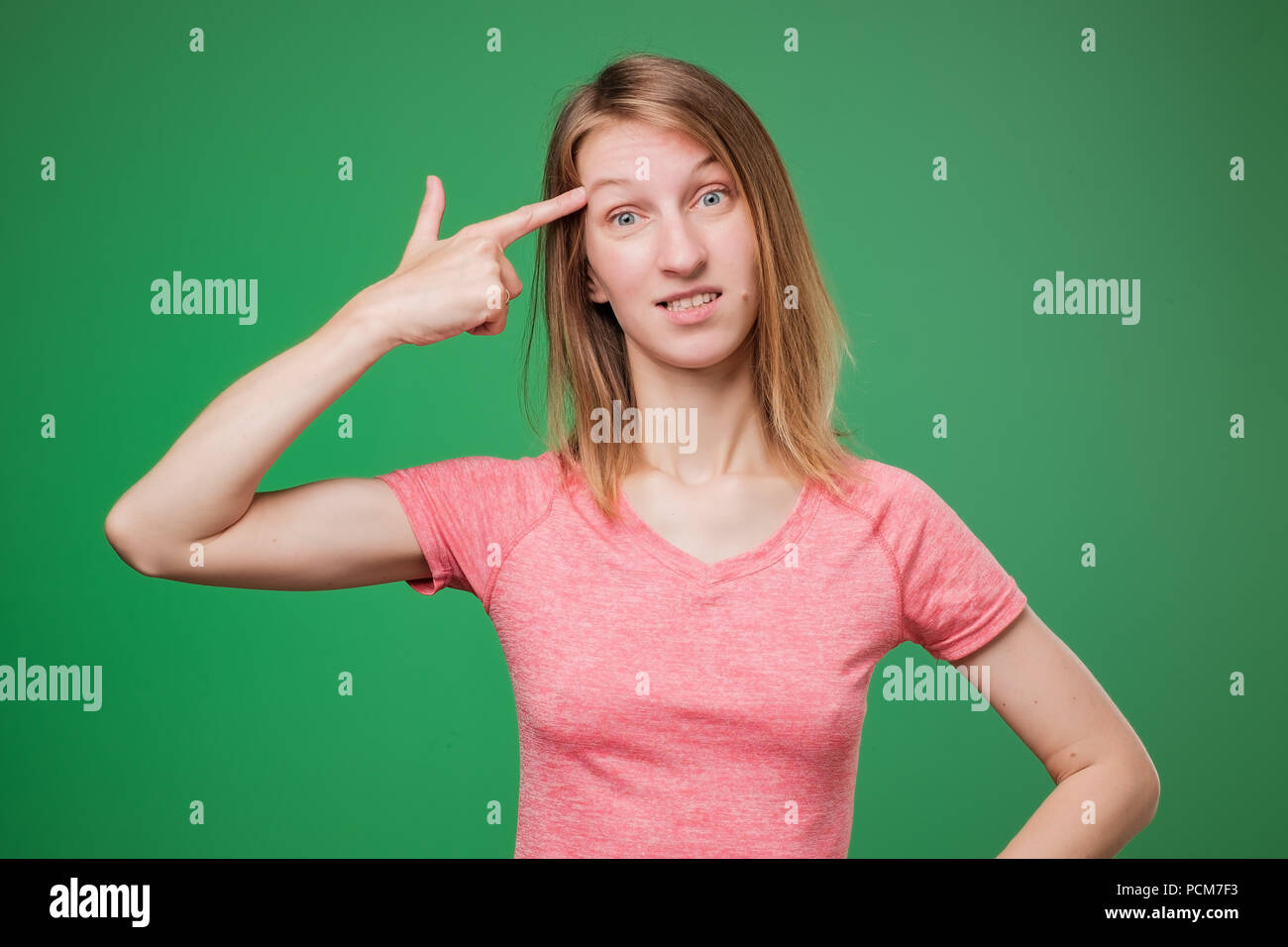 Image of european woman emotionally putting fingers to her temple like gun, being puzzled over green wall. Stock Photo