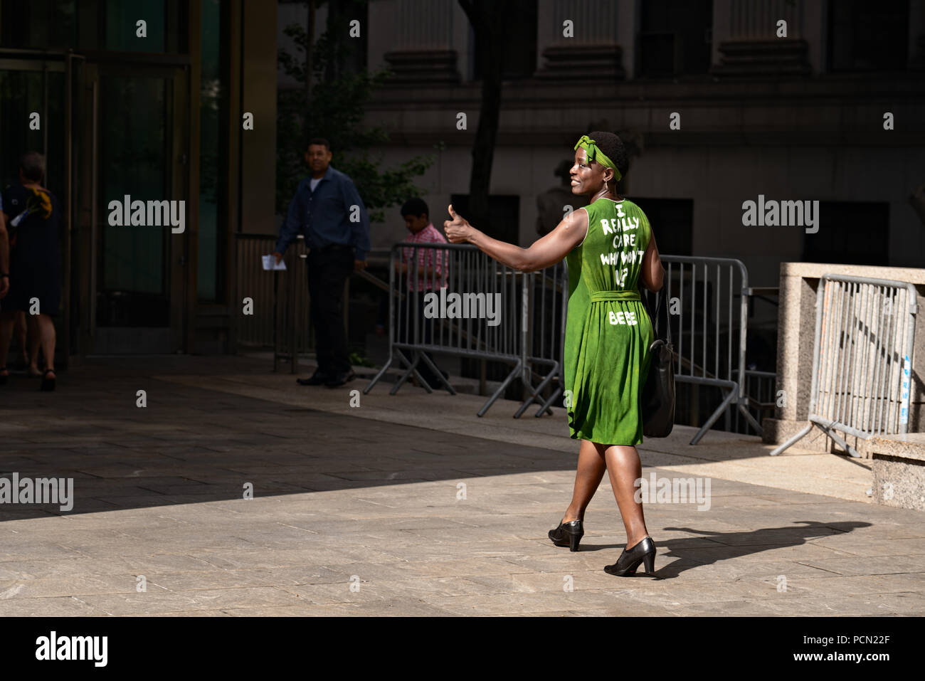 New York, New York, U.S., 3 August 2018 Immigration activist Therese Patricia Okoumou gives a thumbs-up to supporters as she walks into federal court in Manhattan before a hearing on trespassing and disorderly conduct charges.  Okoumou scaled the base of the Statue of Liberty on July 4, 2018, to protest against Trump administration immigration policies.  Okoumou wore a green dress to court bearing the words “I really care why won’t u?” – a response to first lady Melania Trump, who wore a jacket with the words “I really don’t care, do u?” when she visited a facility for migrant children in June Stock Photo