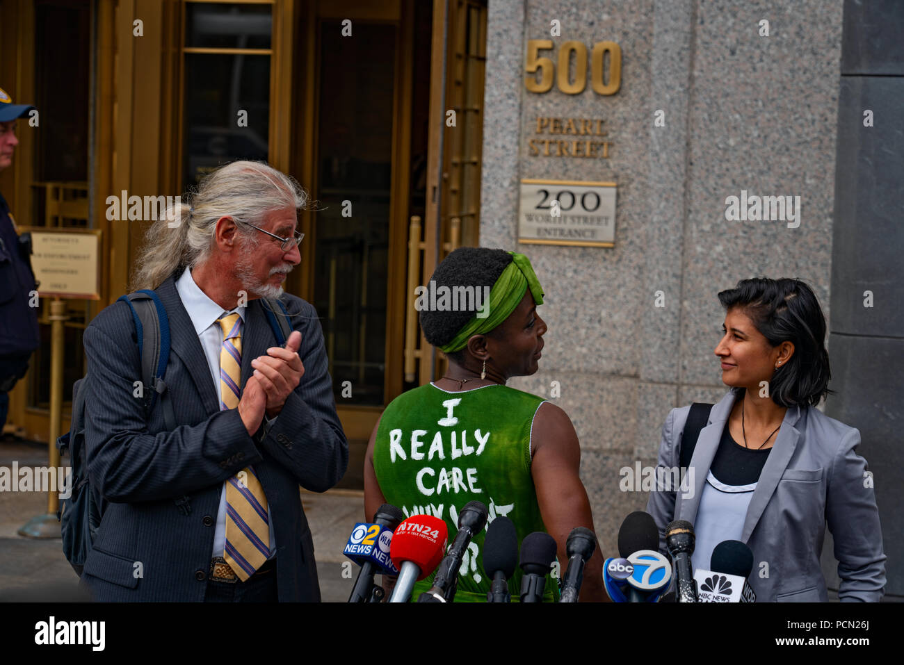 New York, New York, U.S., 3 August 2018 Immigration activist Therese Patricia Okoumou, with lawyers at her side, speaks outside federal court in Manhattan after hearing on trespassing & disorderly conduct charges.  Okoumou, a Congo native, scaled base of Statue of Liberty on July 4, 2018, to protest against Trump administration immigration policies.  Okoumou wore a green dress to court bearing the words “I really care why won’t u?” – a response to first lady Melania Trump, who wore a jacket with the words “I really don’t care, do u?” when she visited a facility for migrant children in June. Stock Photo