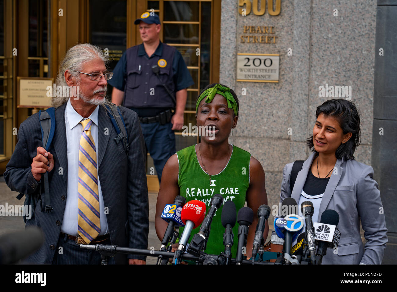 New York, New York, U.S., 3 August 2018 Immigration activist Therese Patricia Okoumou, with lawyers at her side, speaks outside federal court in Manhattan after hearing on trespassing & disorderly conduct charges.  Okoumou, a Congo native, scaled base of Statue of Liberty on July 4, 2018, to protest against Trump administration immigration policies.  Okoumou wore a green dress to court bearing the words “I really care why won’t u?” – a response to first lady Melania Trump, who wore a jacket with the words “I really don’t care, do u?” when she visited a facility for migrant children in June. Stock Photo