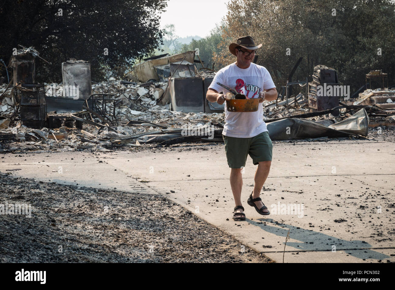Redding, California, USA. 3rd Aug, 2018. ALISTAIR SULLIVAN pulls items, including a cooking pot, from the remnants of his home that burned in the Carr Fire. Sullivan, who has lived in the Lake Redding Estates area for approximately three years, remains optimistic. He's currently staying in a local hotel and has set up a fundraising page on Facebook to help defray some of the costs needed to rebuild. The Carr Fire has killed six people and destroyed more than a thousand homes and buildings since it raged through the area last week. Credit: Tracy Barbutes/ZUMA Wire/Alamy Live News Stock Photo